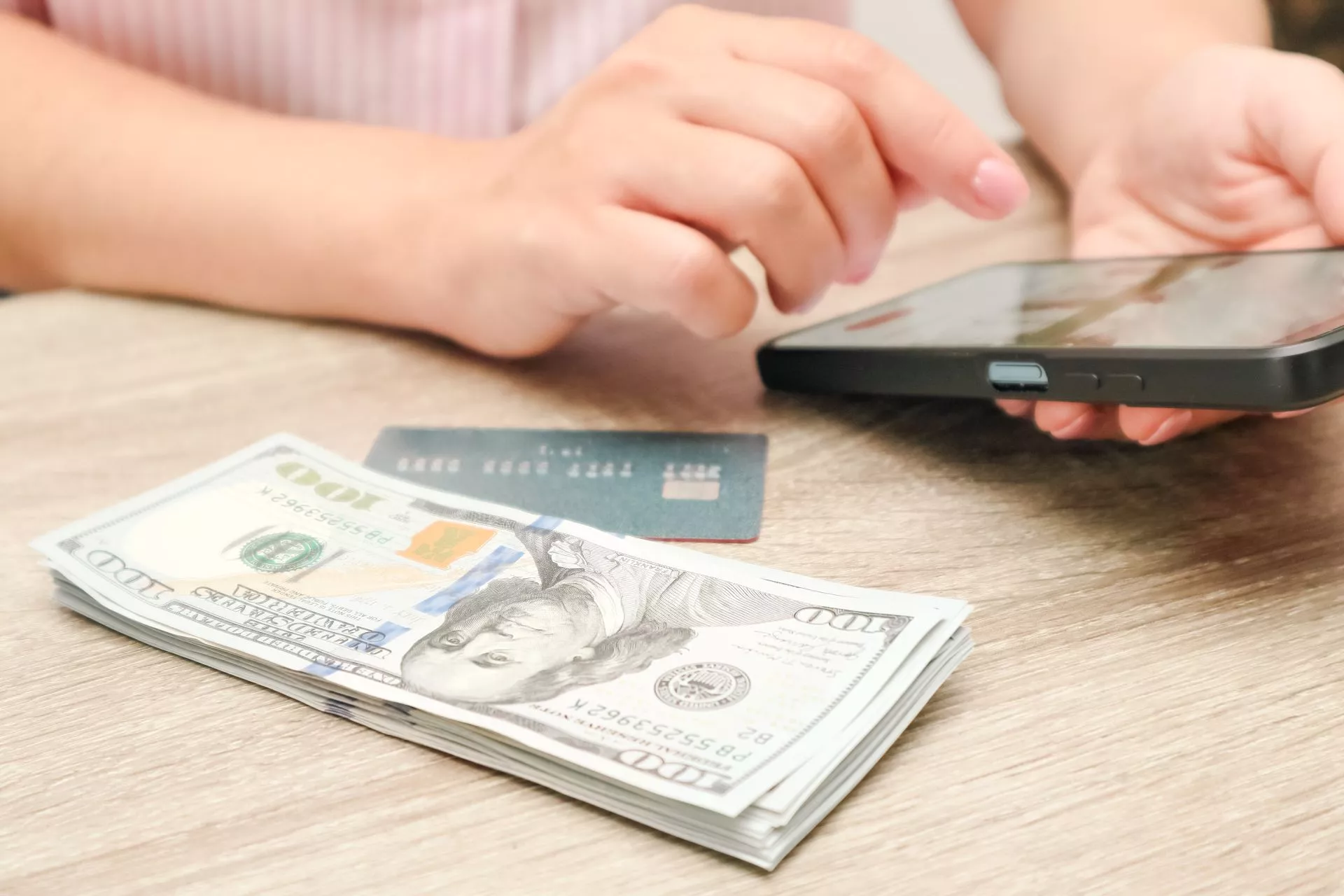 手持手機操作線上刷卡換現金流程，桌上放有信用卡與美元現金，呈現資金周轉、信用卡換現金與數位支付情境